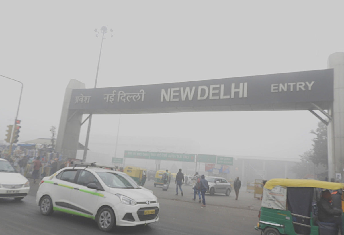 The New Delhi Railway station entry gantry reading NEW DELHI barely visible through thick smog on 31 December 2017, with cars, an auto-rickshaw and pedestrians in the haze